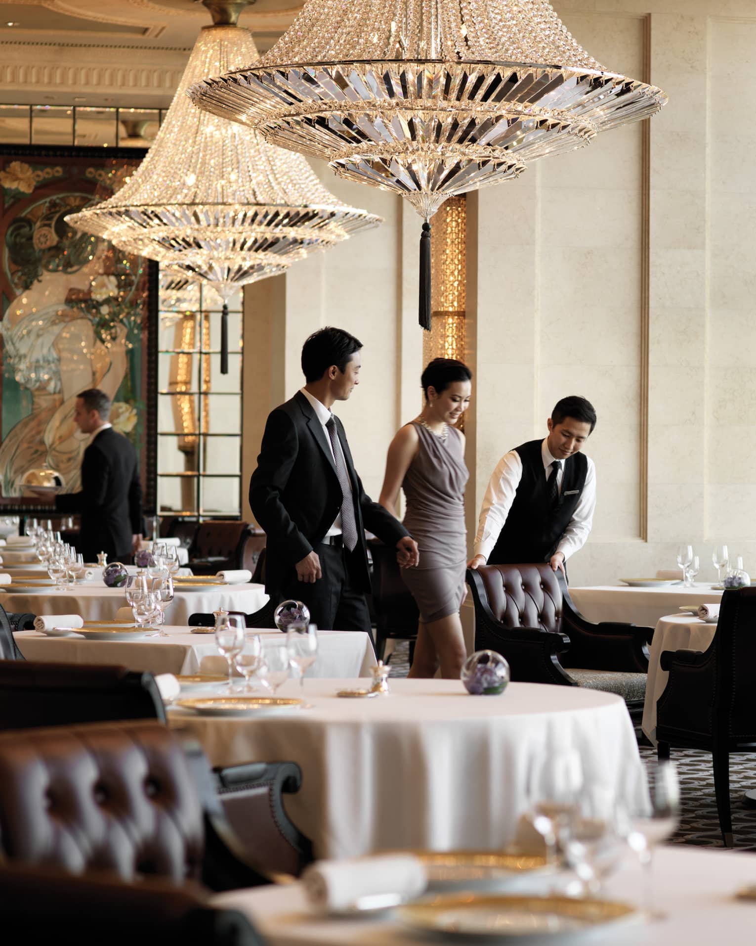 A male waiter pulls a leather seat out at a dining table for a woman