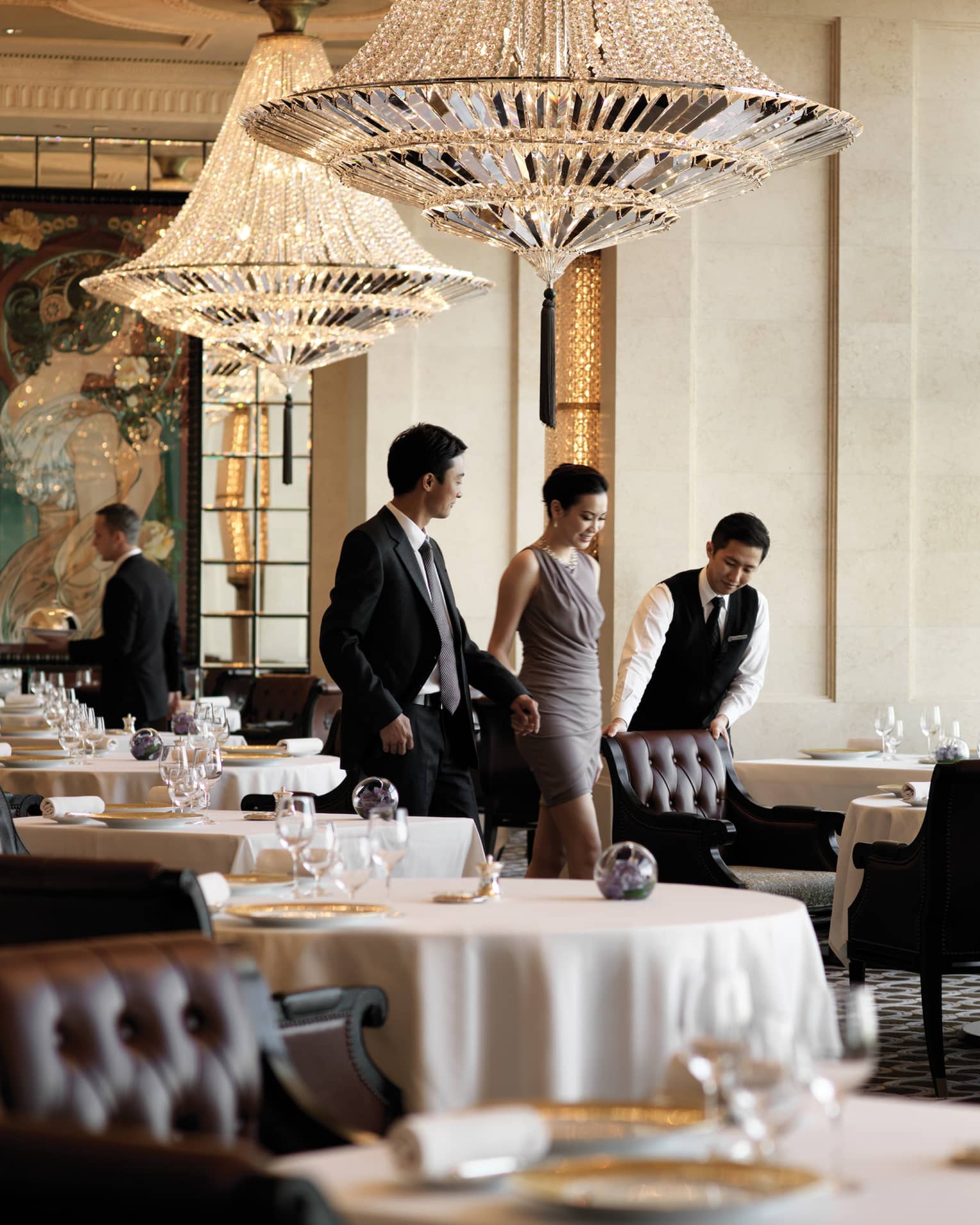 A male waiter pulls a leather seat out at a dining table for a woman