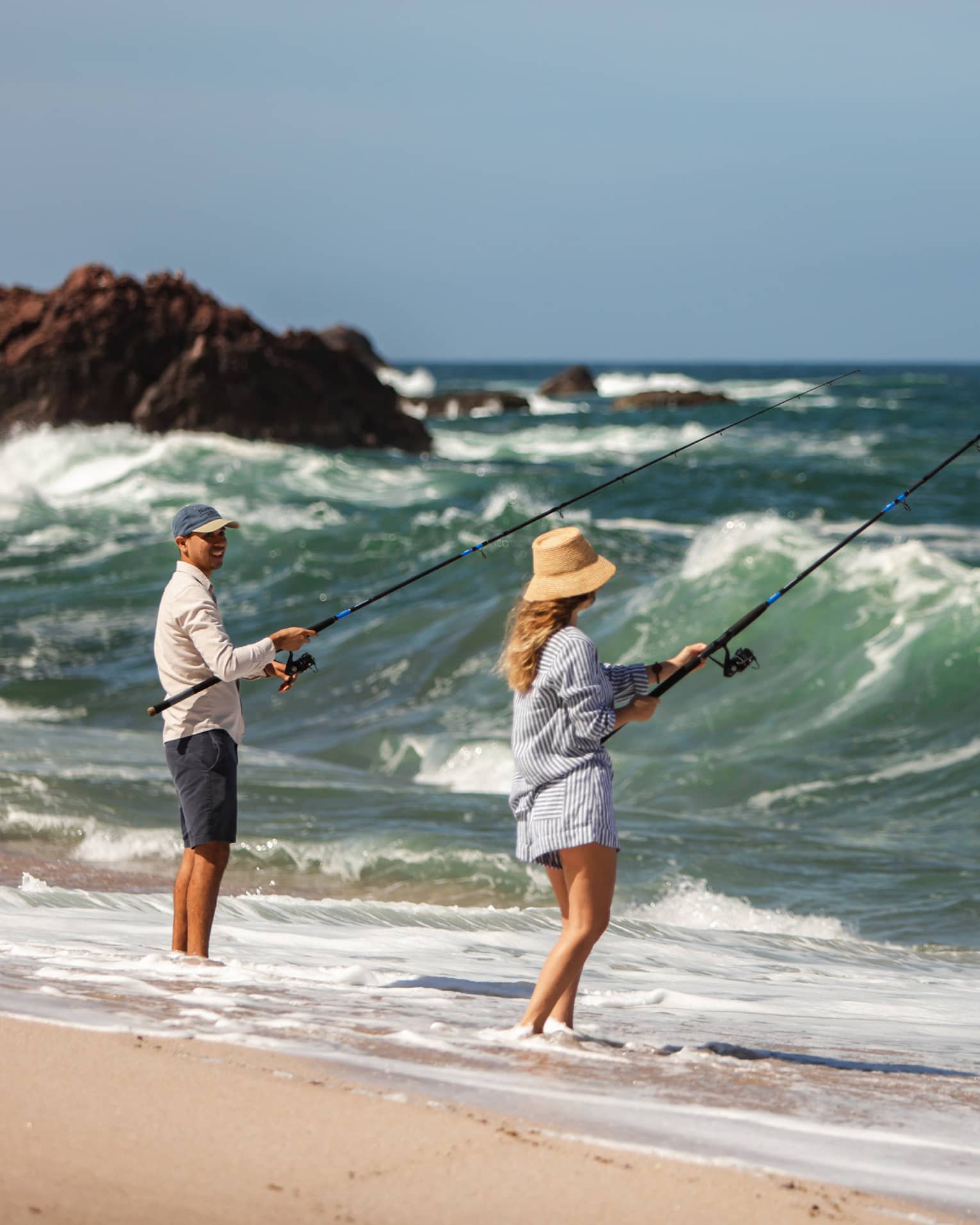 Two people fishing on a beach shore.