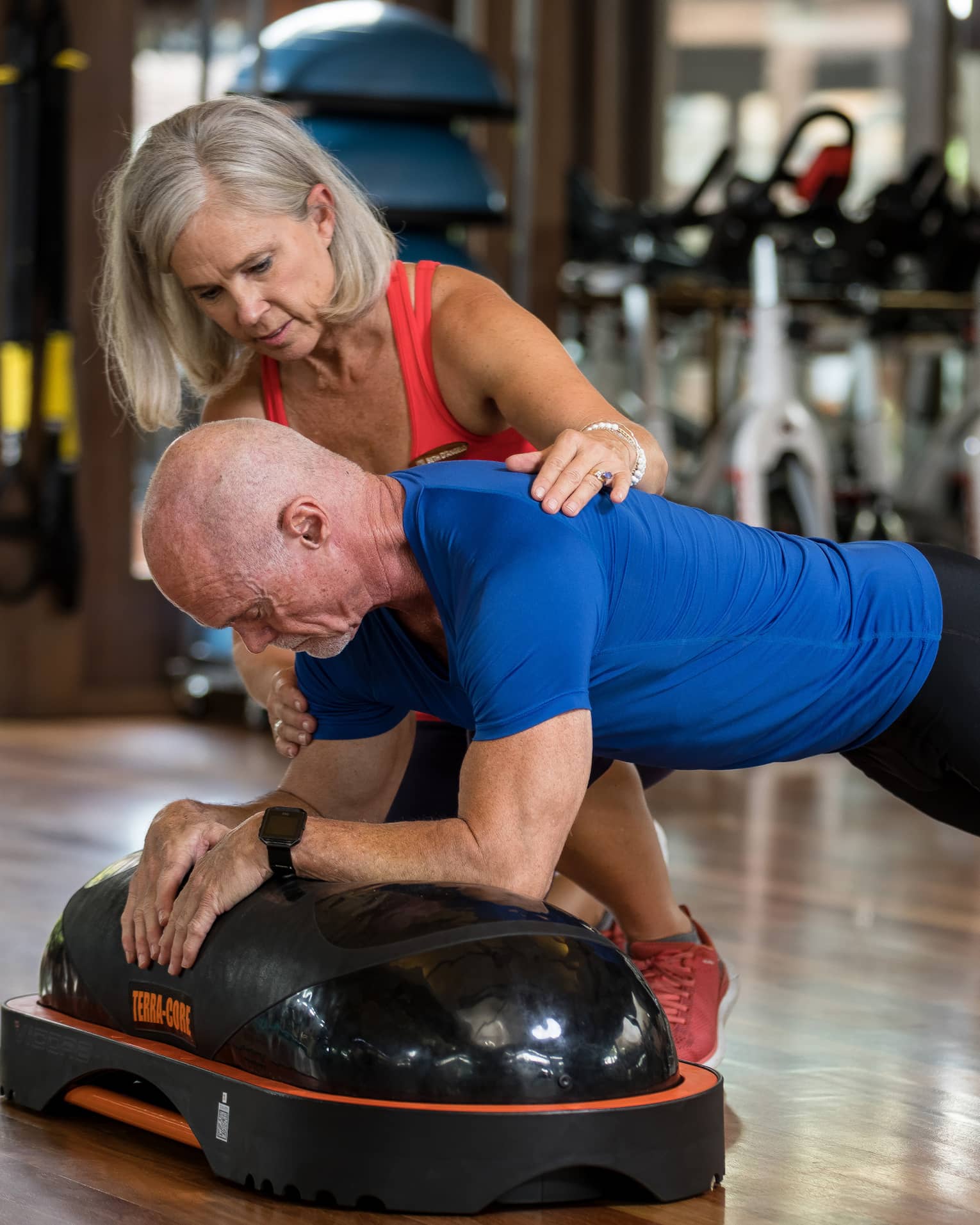 Fitness trainer helps man balance on pilates board in exercise studio