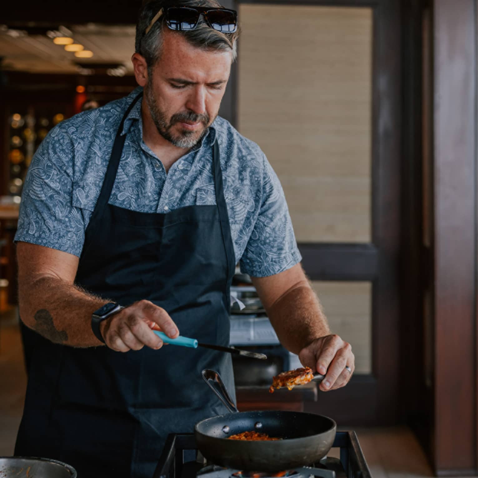 Man wear black apron cooks over a burner
