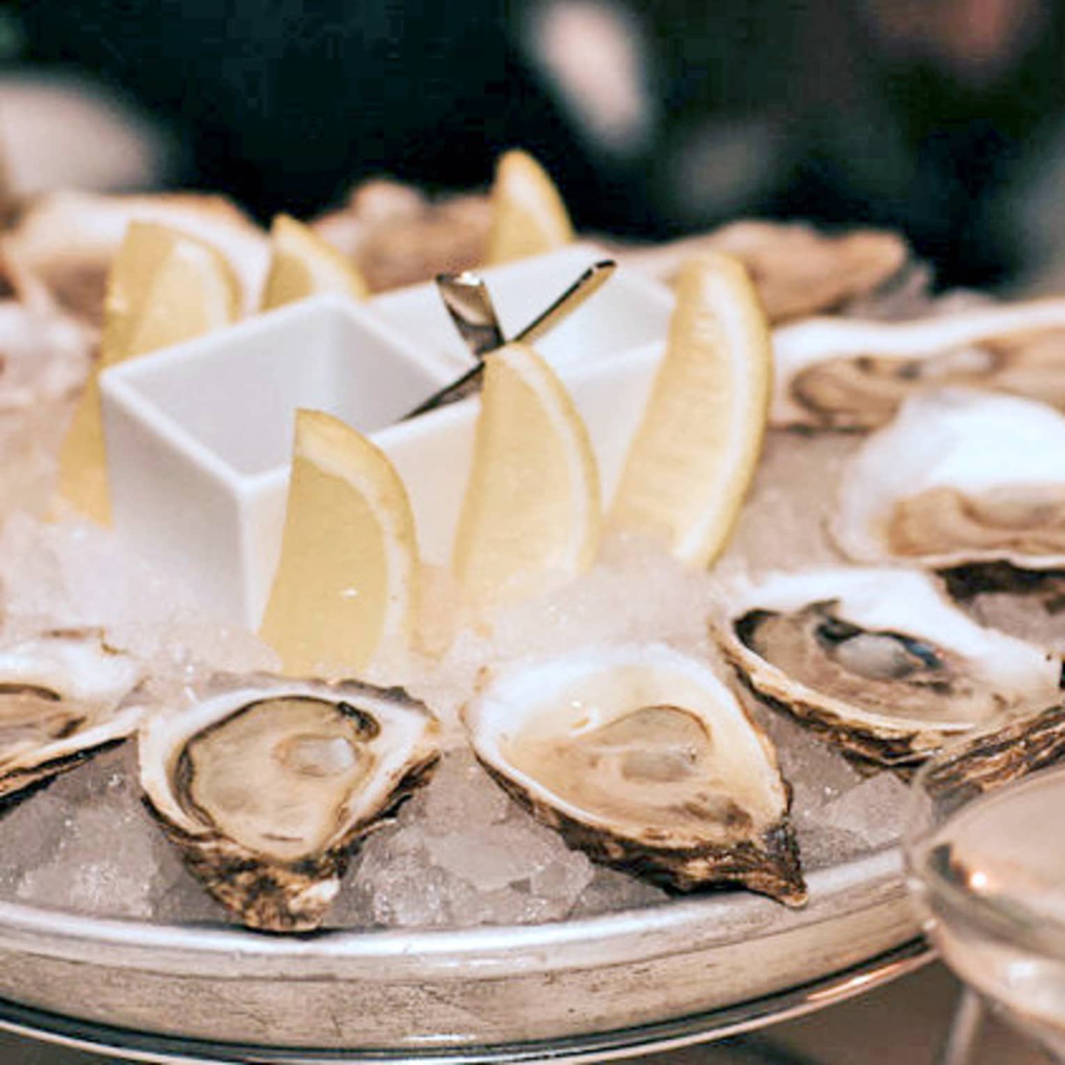 A dozen raw oysters around an ice platter with three lemon wedges in centre