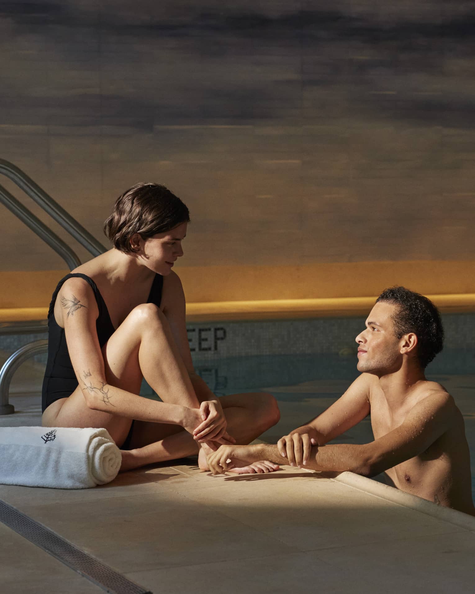 Person sitting poolside with a towel talking to another person leaning on the edge of the pool at Four Seasons luxury hotel