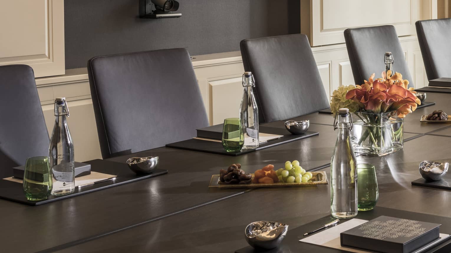 Long boardroom table set with glass bottles of water, flowers in bright meeting room