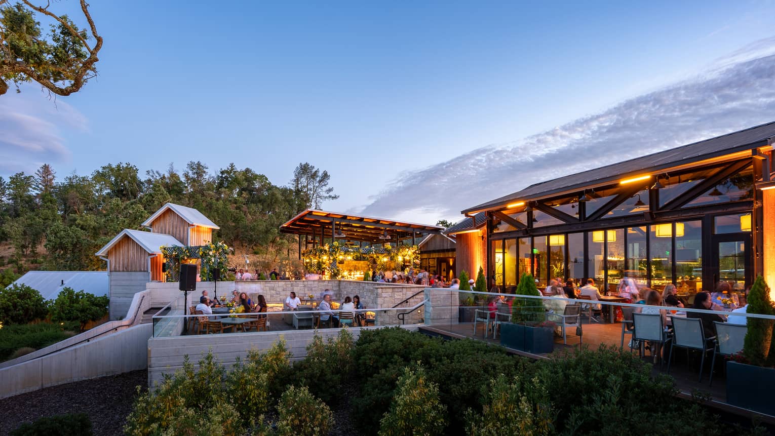 A patio with guests sitting at dining tables below soft lighting