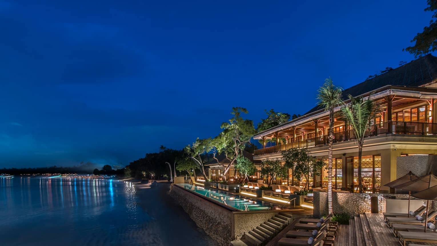 Exterior view of Sundara restaurant, swimming pool lit up at night, in front of dark beach, ocean