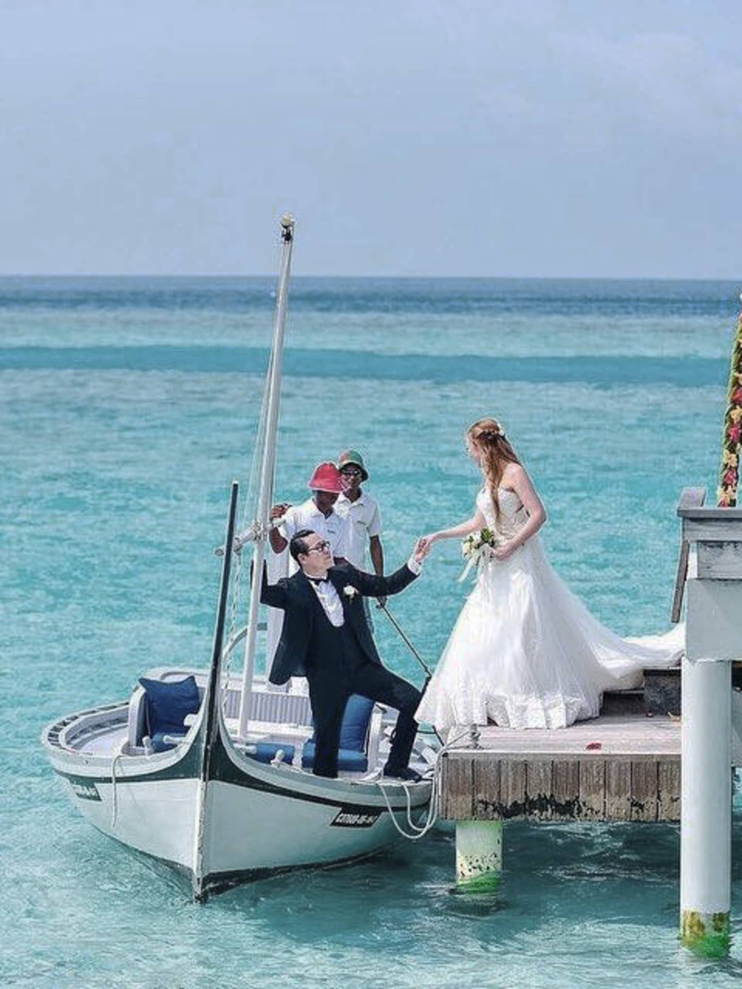 Groom helps bride into canoe at dock of overwater wedding ceremony on lagoon