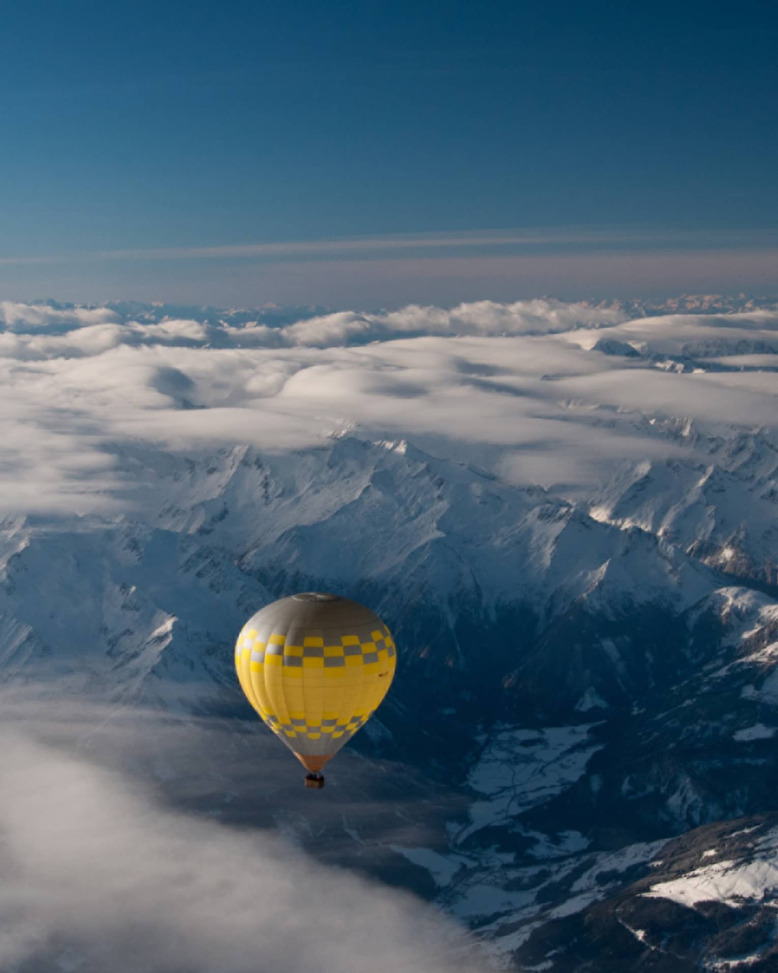 Yellow hot air balloon soaring over the snow-covered Alps