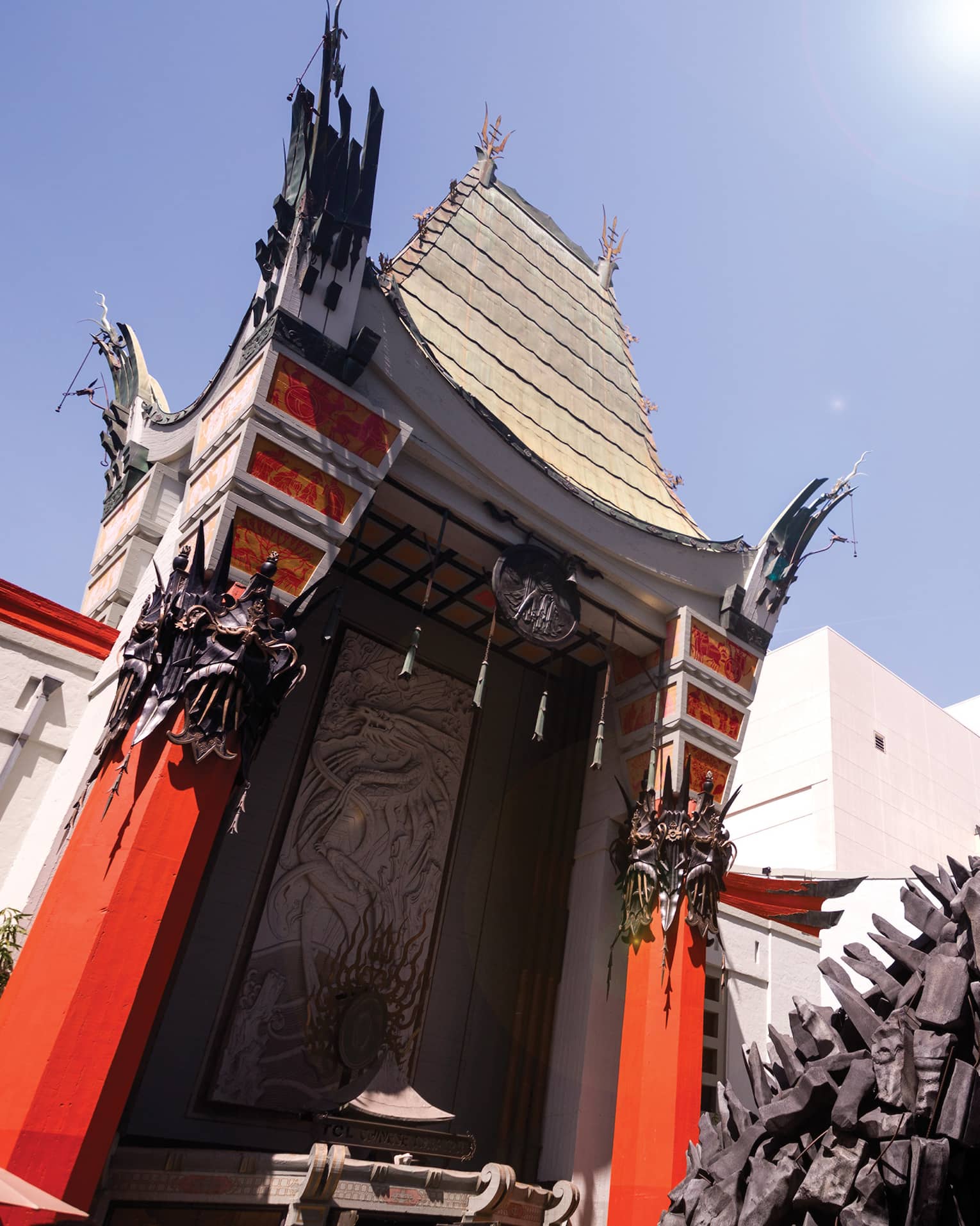 Towering into the sky, a curvy red and white building decorated with Chinese motifs stands behind a large statue of Godzilla.
