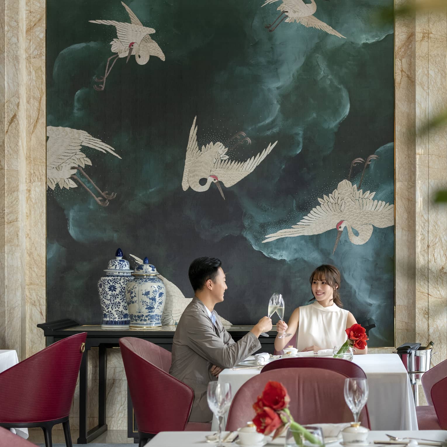 Man and woman clink glasses at table in Zi Yat Heen restaurant at Four Seasons Hotel Macao Cotai Strip