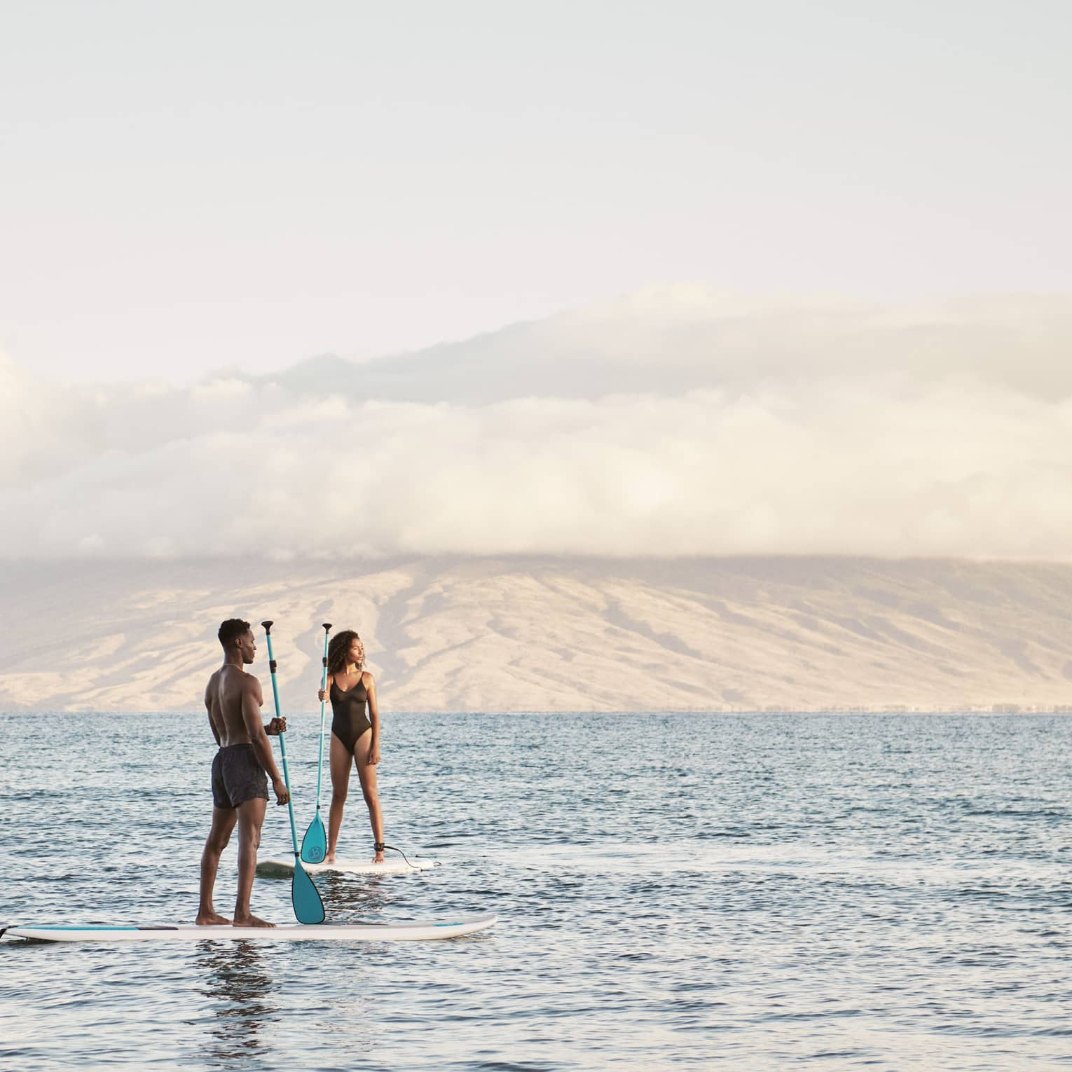 Man and woman stand on SUP paddleboards in the ocean in Maui