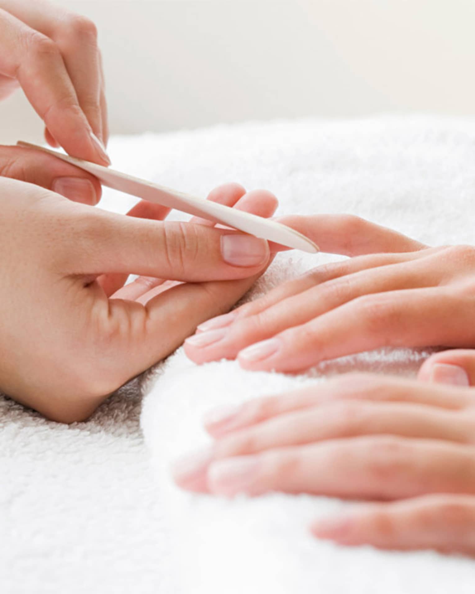 Close-up of spa attendant filing nails of woman's hands as they rest on white towel