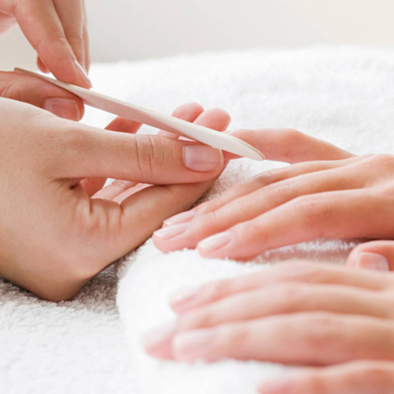 Close-up of spa attendant filing nails of woman's hands as they rest on white towel
