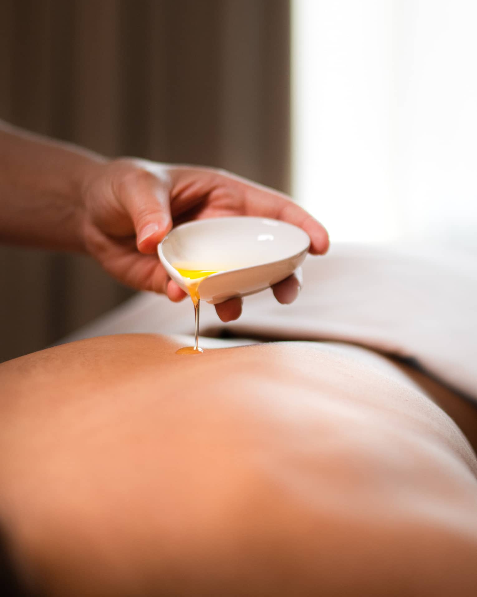 A spa staff member pouring liquid onto a woman?s back.