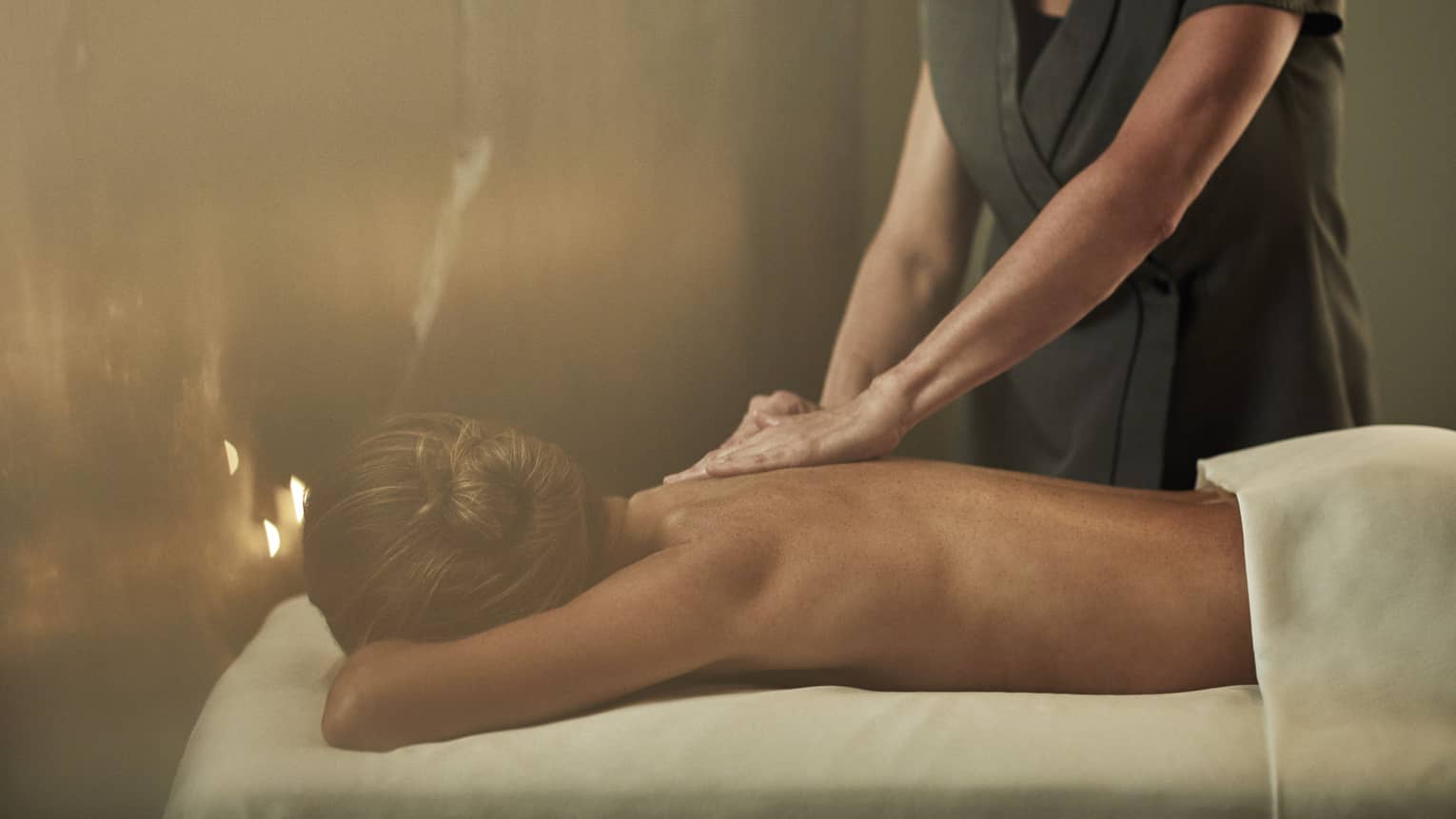 A woman laying on a massage bed being given a massage by a staff member.