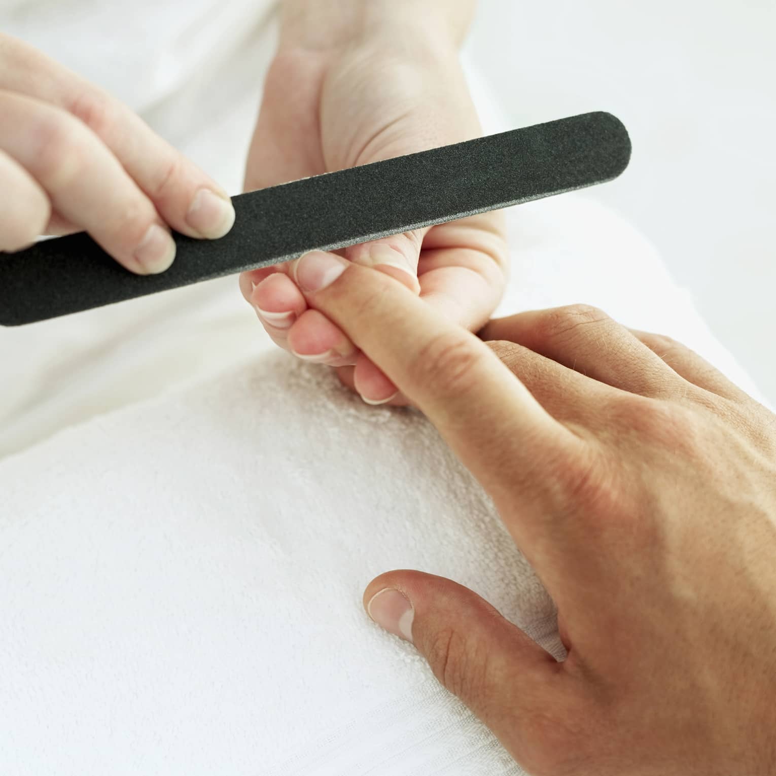 Woman holds manicure nail file to man's fingernails over white towel