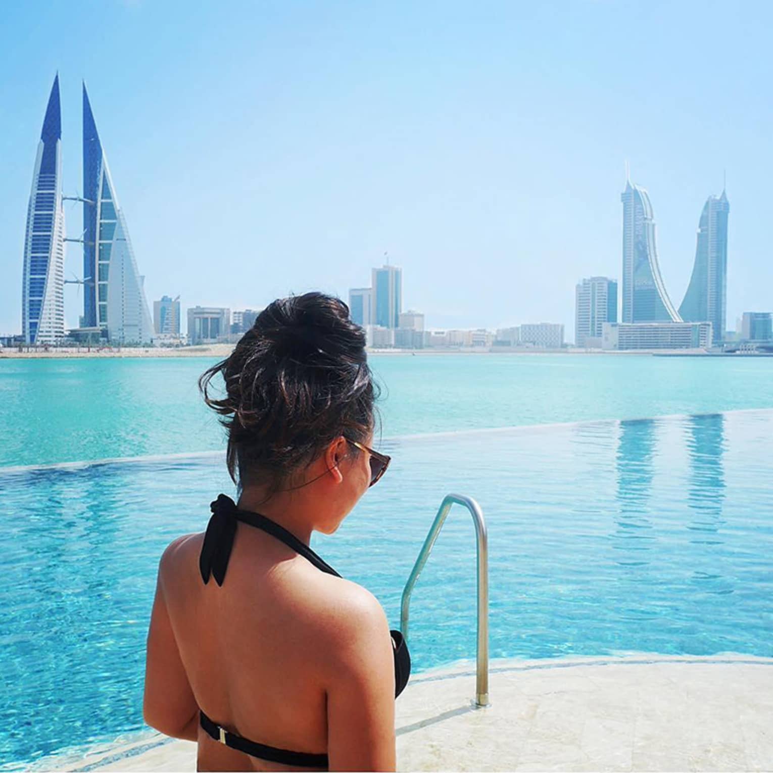Woman in pool with Bahrain city view