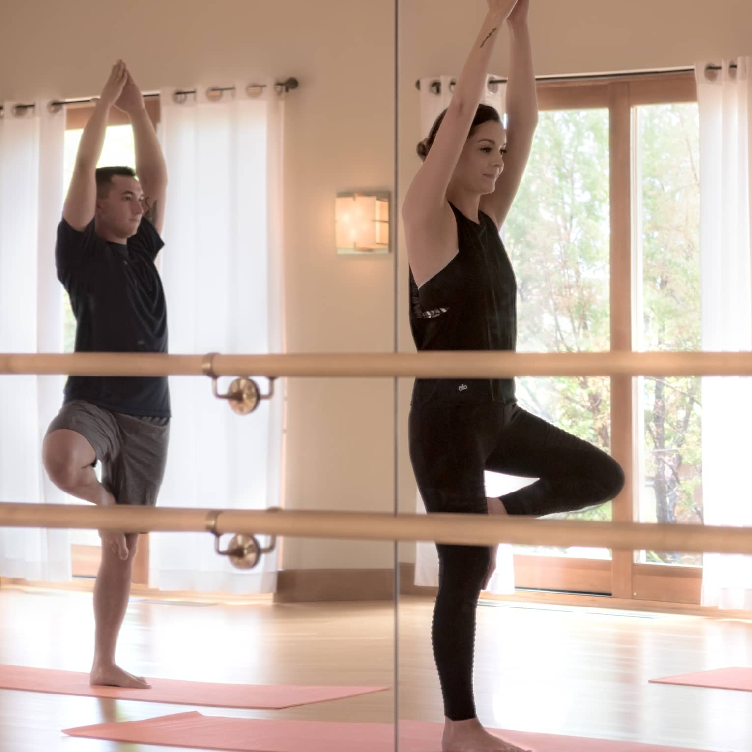 Mirror reflection of three people standing in yoga pose on mats in fitness centre