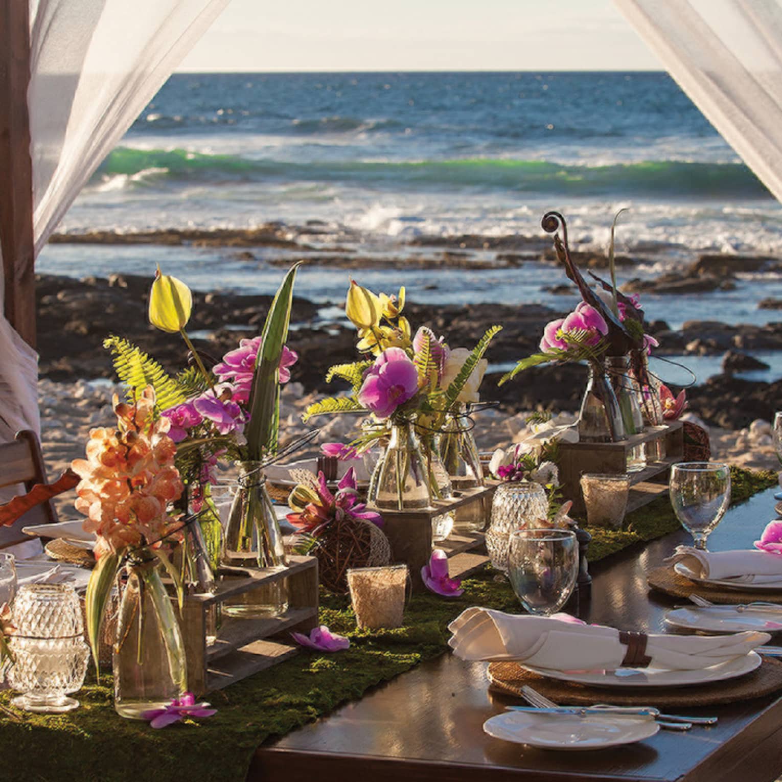 Private beach dining table with floral arrangements and sheer curtains