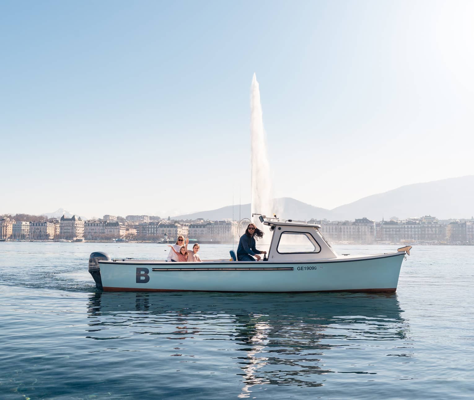 Four people in small boat on Lake Geneva with Jet d'Eau fountain and city in backdrop