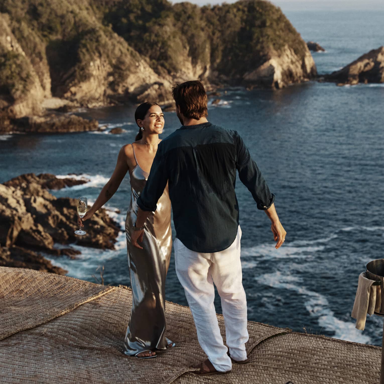 A couple standing near a vast, shimmering ocean against a backdrop of majestic cliffs, embraced by the beauty of nature
