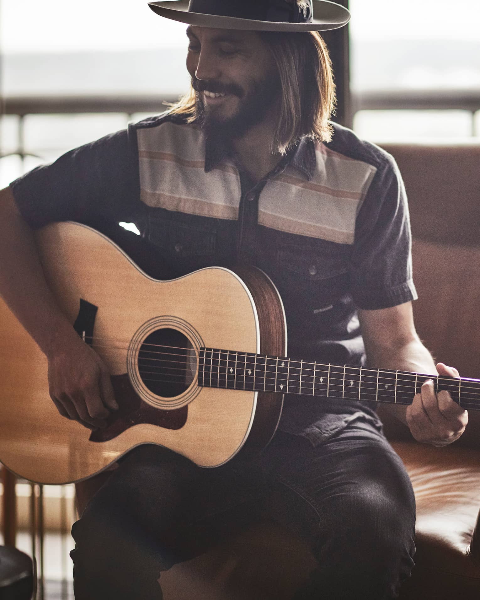 Smiling Guitar Concierge with long hair, beard, hat plays acoustic Taylor guitar