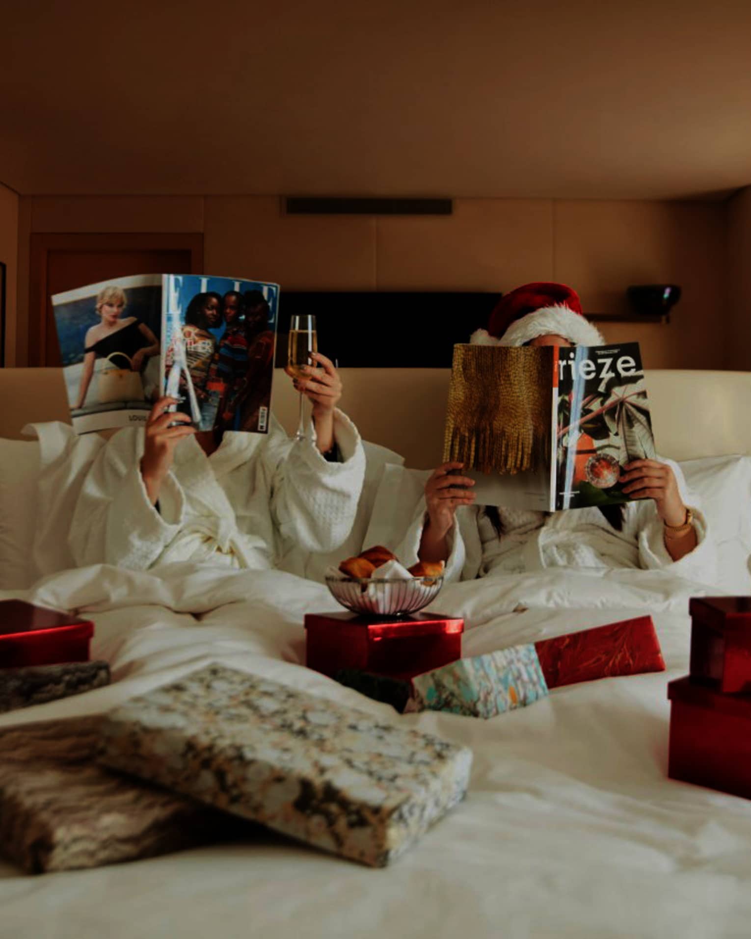 Couple in white bed covered in Christmas gifts, reading magazines