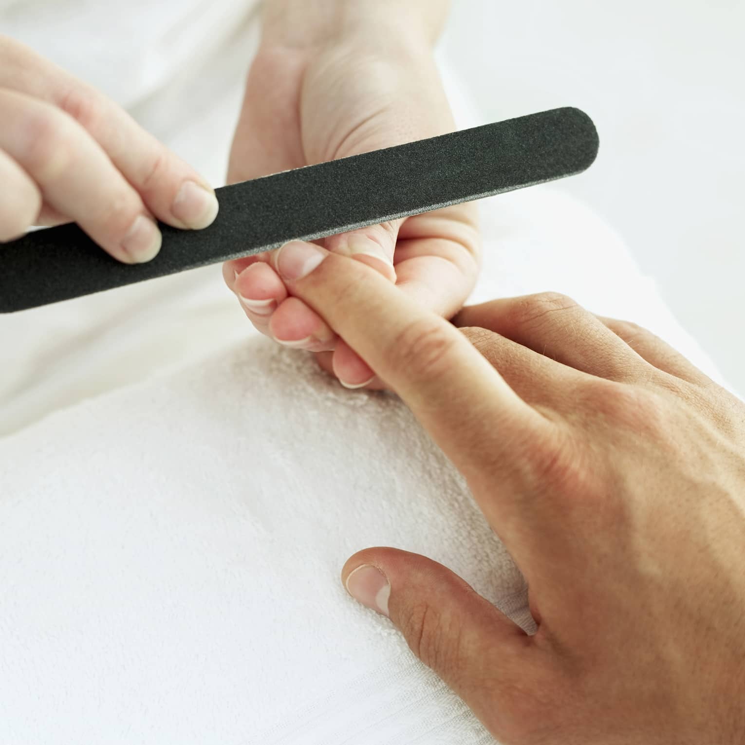 Woman holds manicure nail file to man's fingernails over white towel