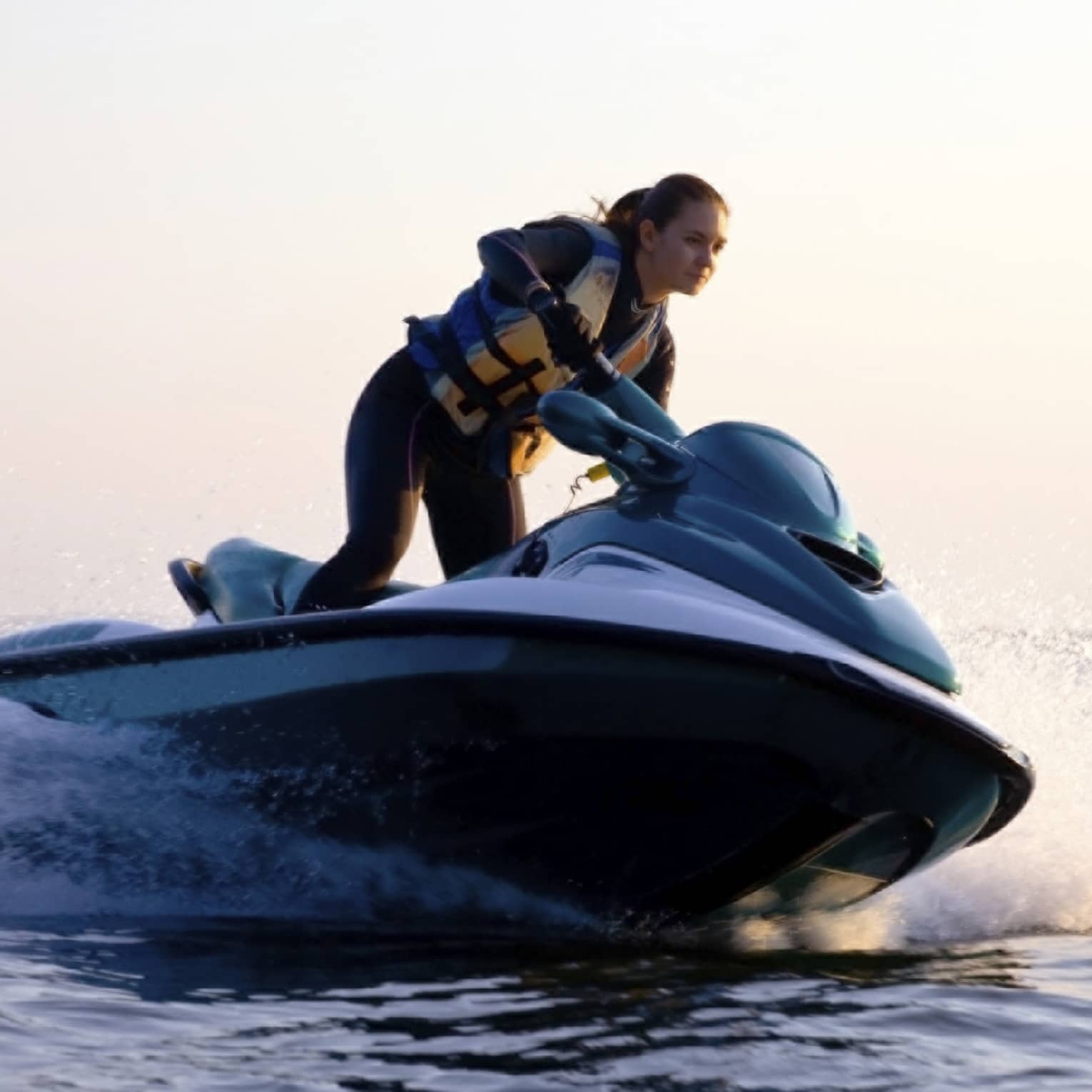 Woman wearing life jacket stands, steers jet ski on ocean at sunset