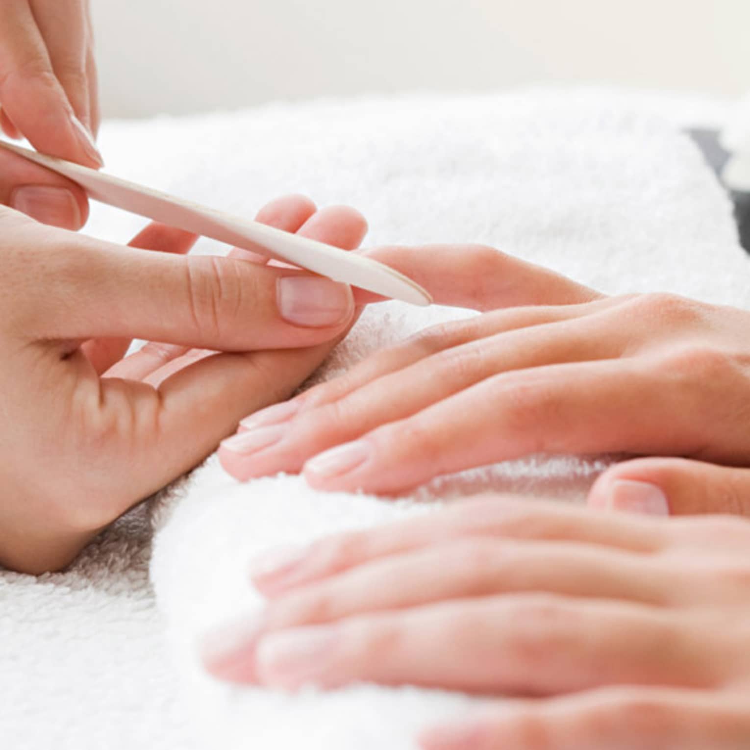 Close-up of spa attendant filing nails of woman's hands as they rest on white towel