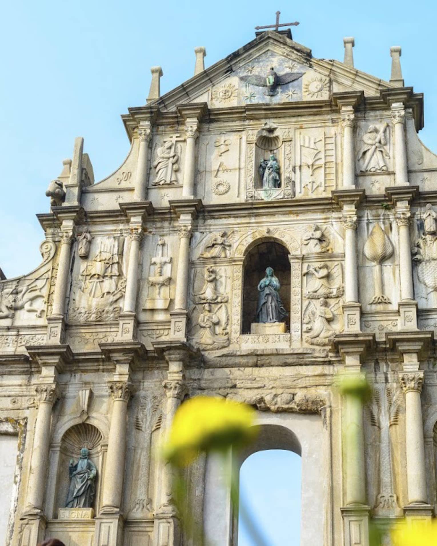 An ornate facade with archways at bottom, lined with thin towers and columns, intricate carvings and shelves holding statues.