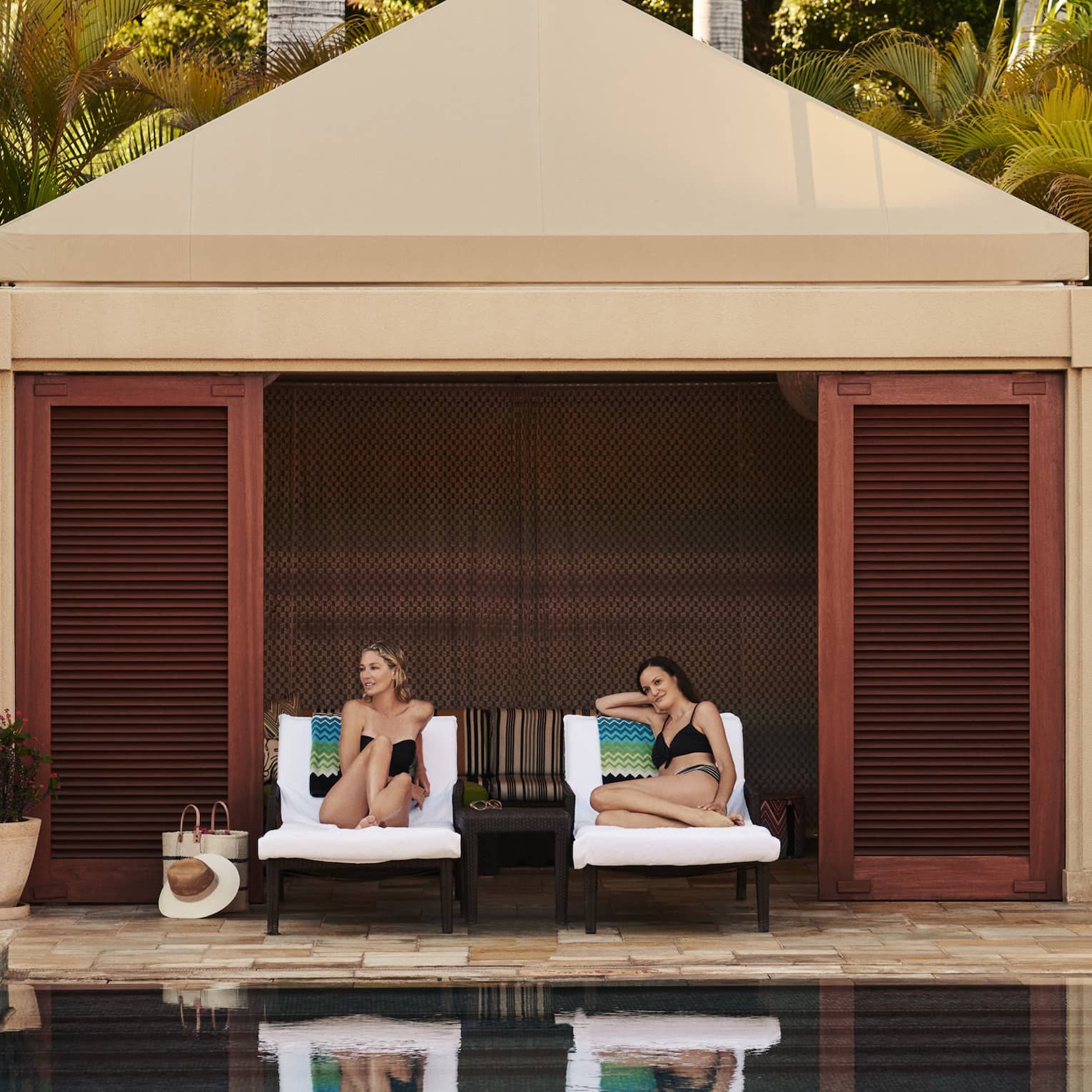 Two women on lounge chairs under poolside cabana