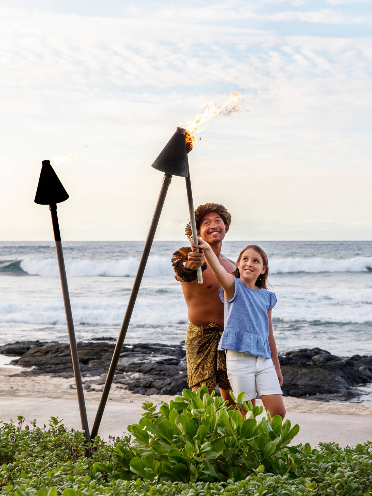 A father and daughter lighting lanterns along a beach shore together.