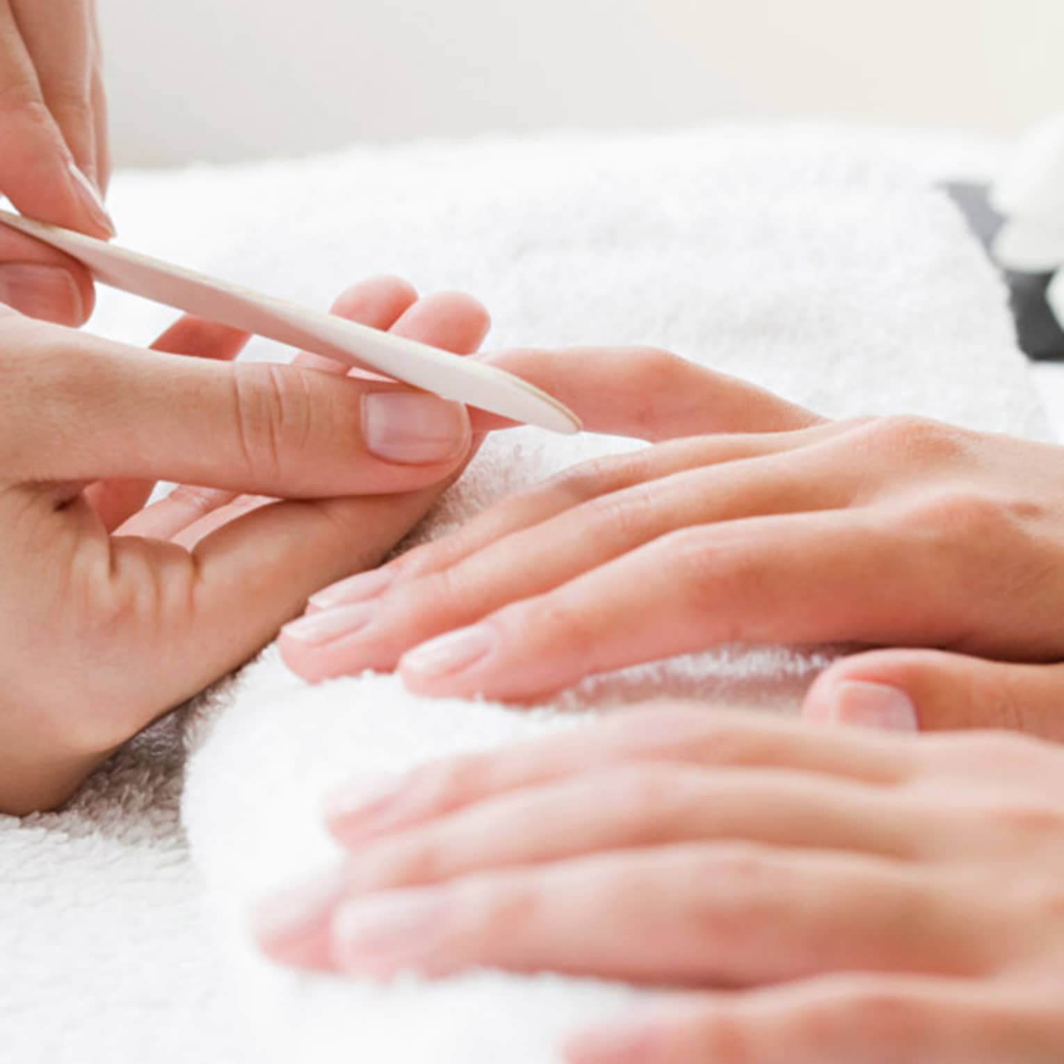 Close-up of spa attendant filing nails of woman's hands as they rest on white towel