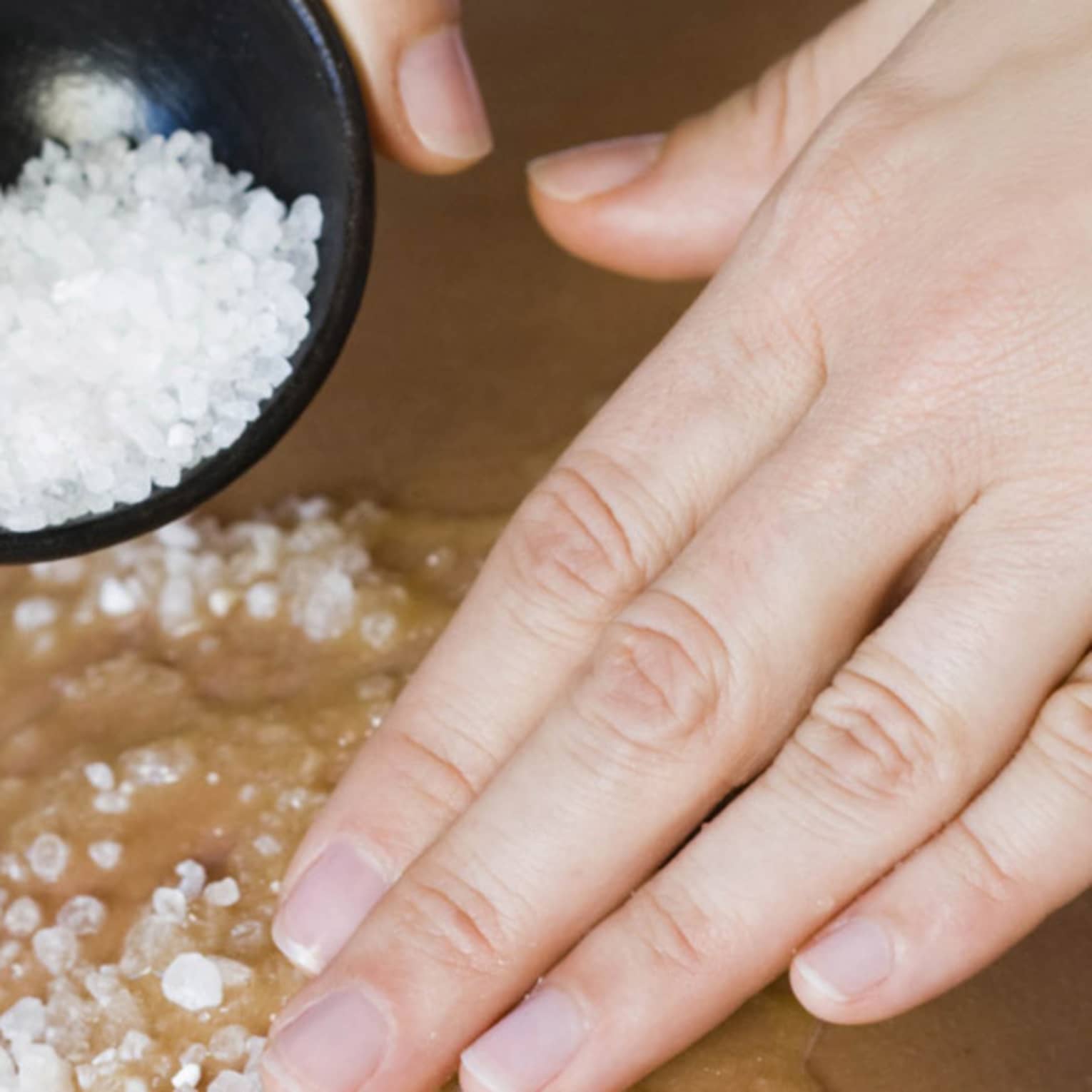Close-up of large spa salts in bowl, hand rubbing crystals on bare back