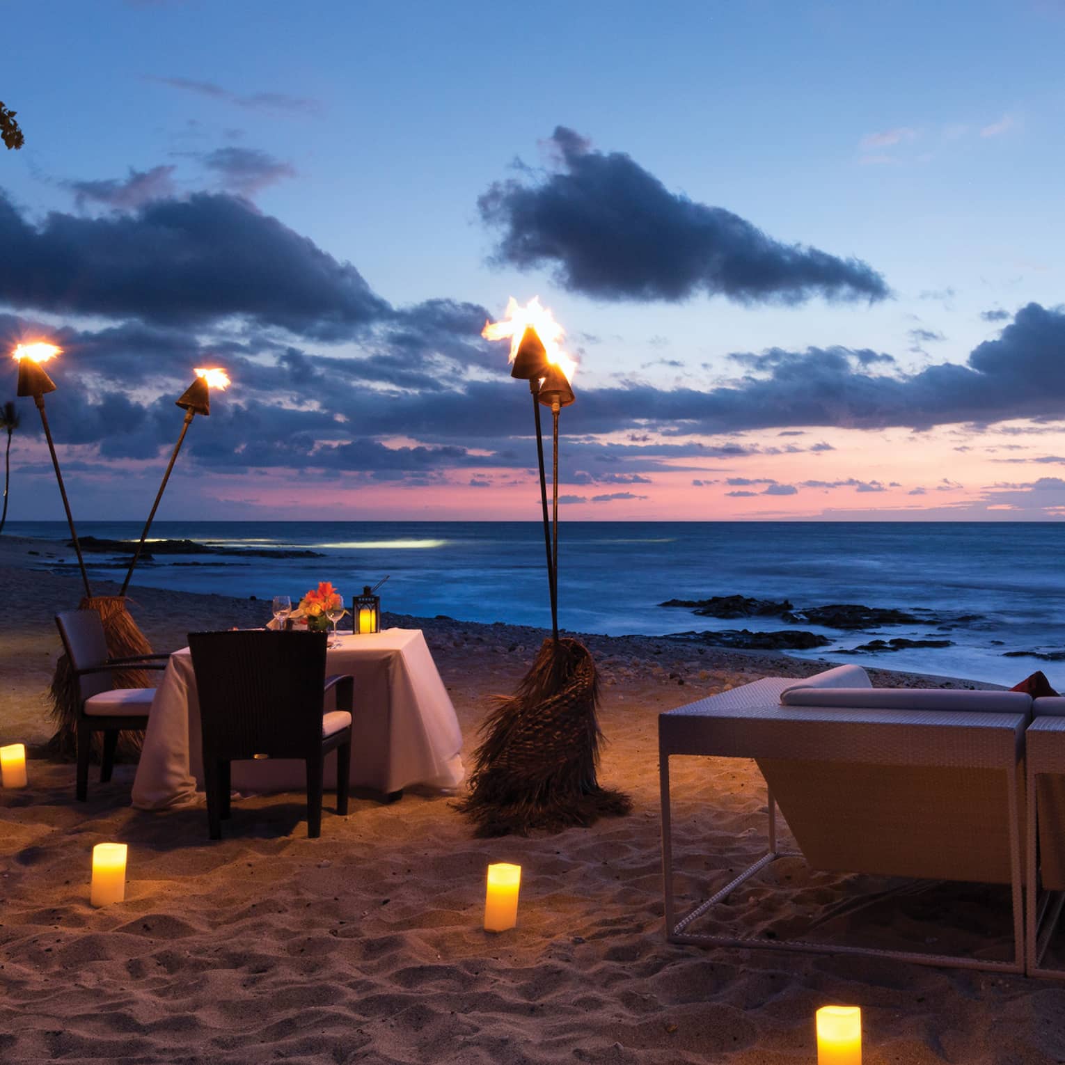 Torches over dining table on beach at night, glowing candles in the sand