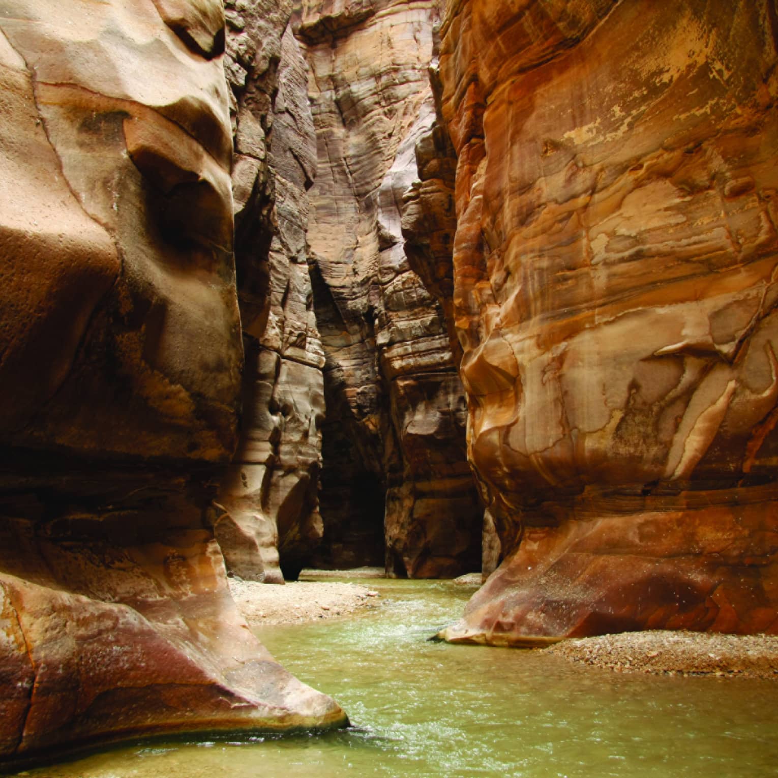 A narrow waterway runs between curved sandstone cliffs in Wadi Mujib