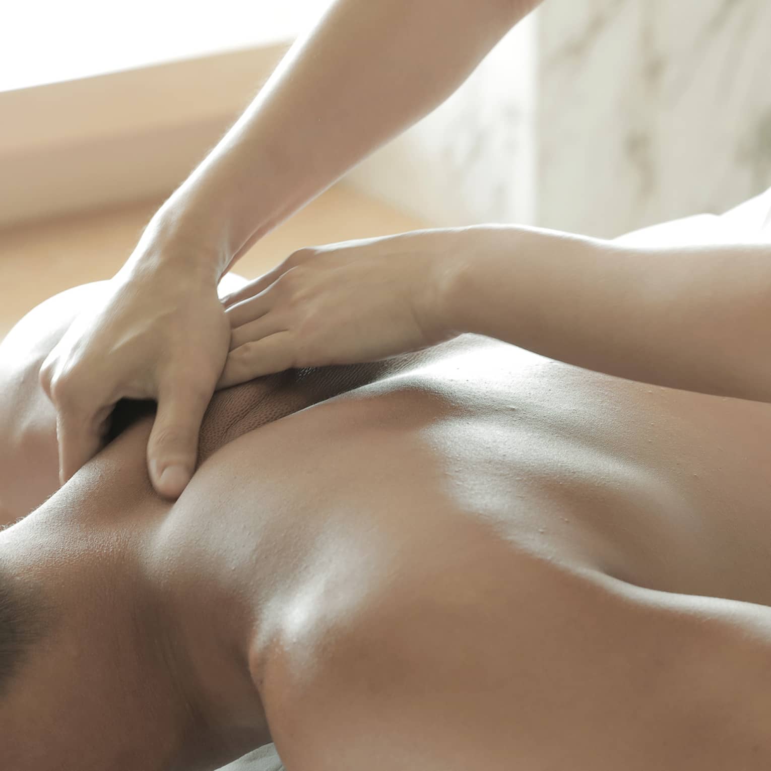 Spa masseuse massages man's bare back, shoulders