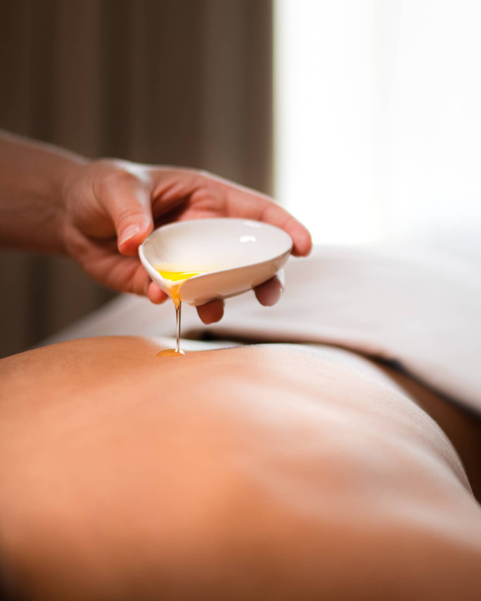 A spa staff member pouring liquid onto a woman?s back.