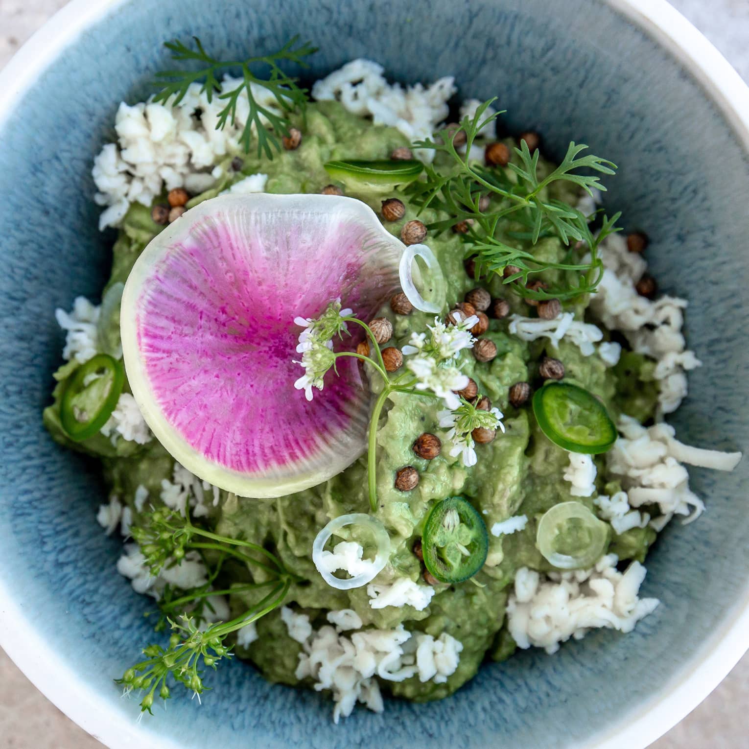A blue bowl with herbs and guacamole in it.