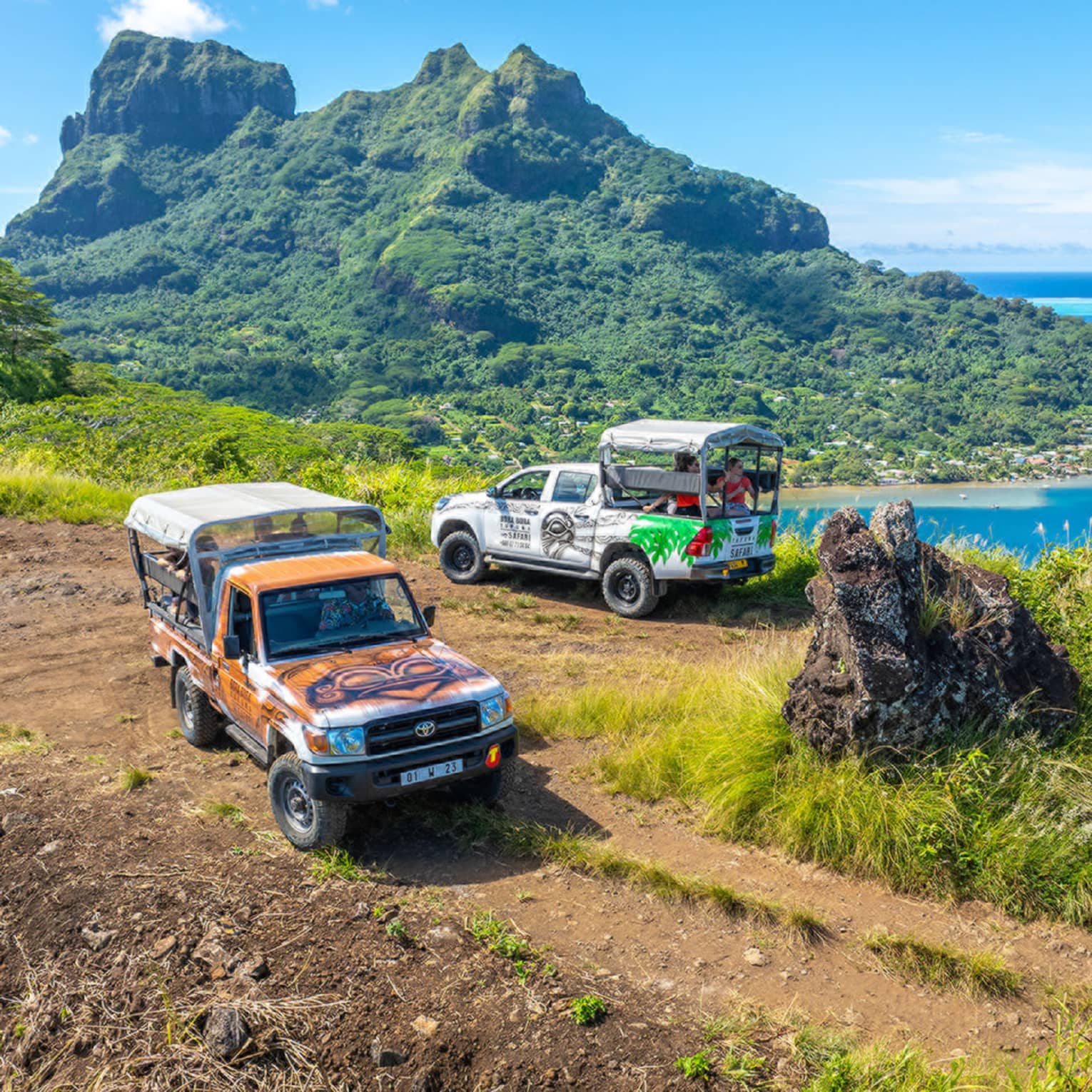 Two trucks parked on dirt path with green mountain looming in background