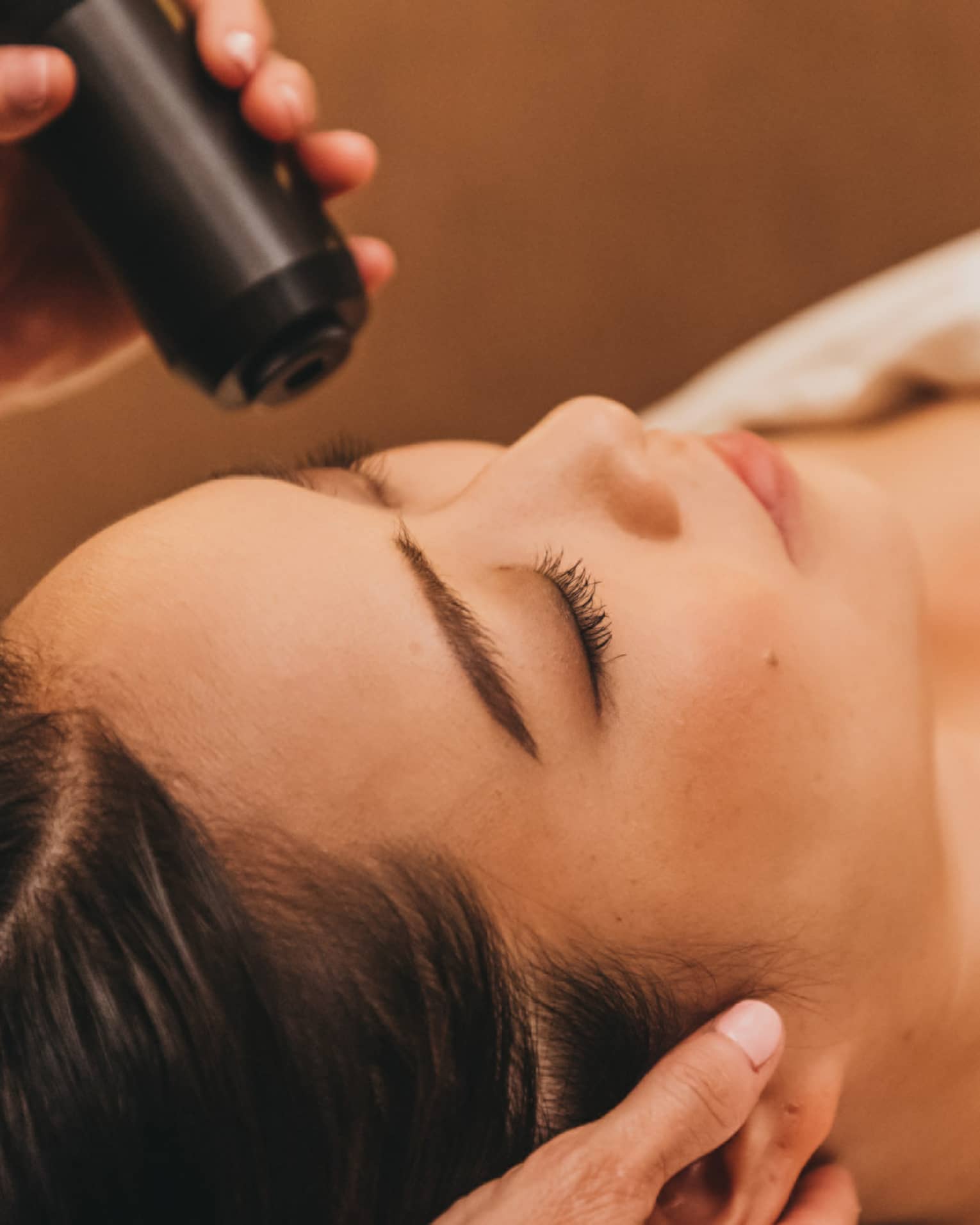 A spa staff member applies a cryotherapy treatment to a woman's forehead