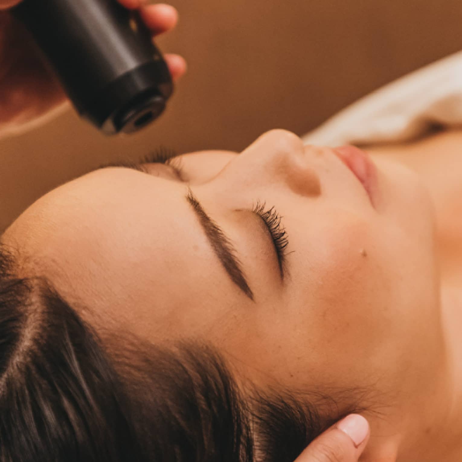 A spa staff member applies a cryotherapy treatment to a woman's forehead