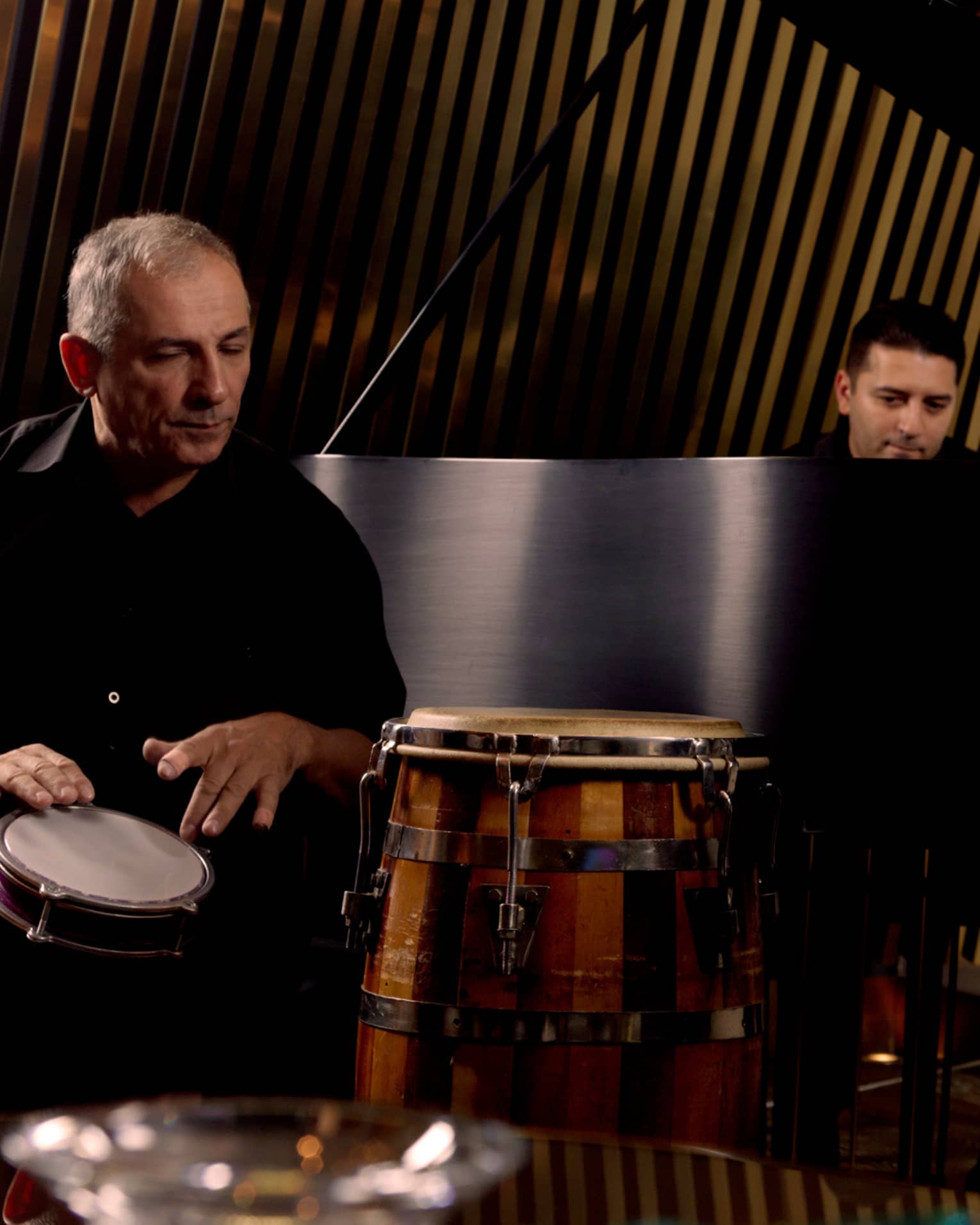 Three band members playing hand drum, grand piano and double bass