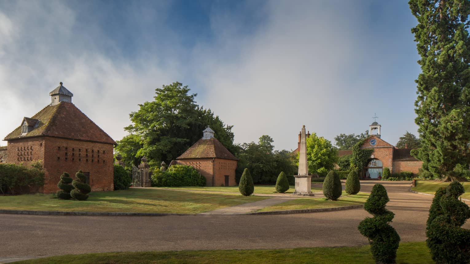 Red brick cottages, small clocktower, landmark on landscaped green gardens, trees