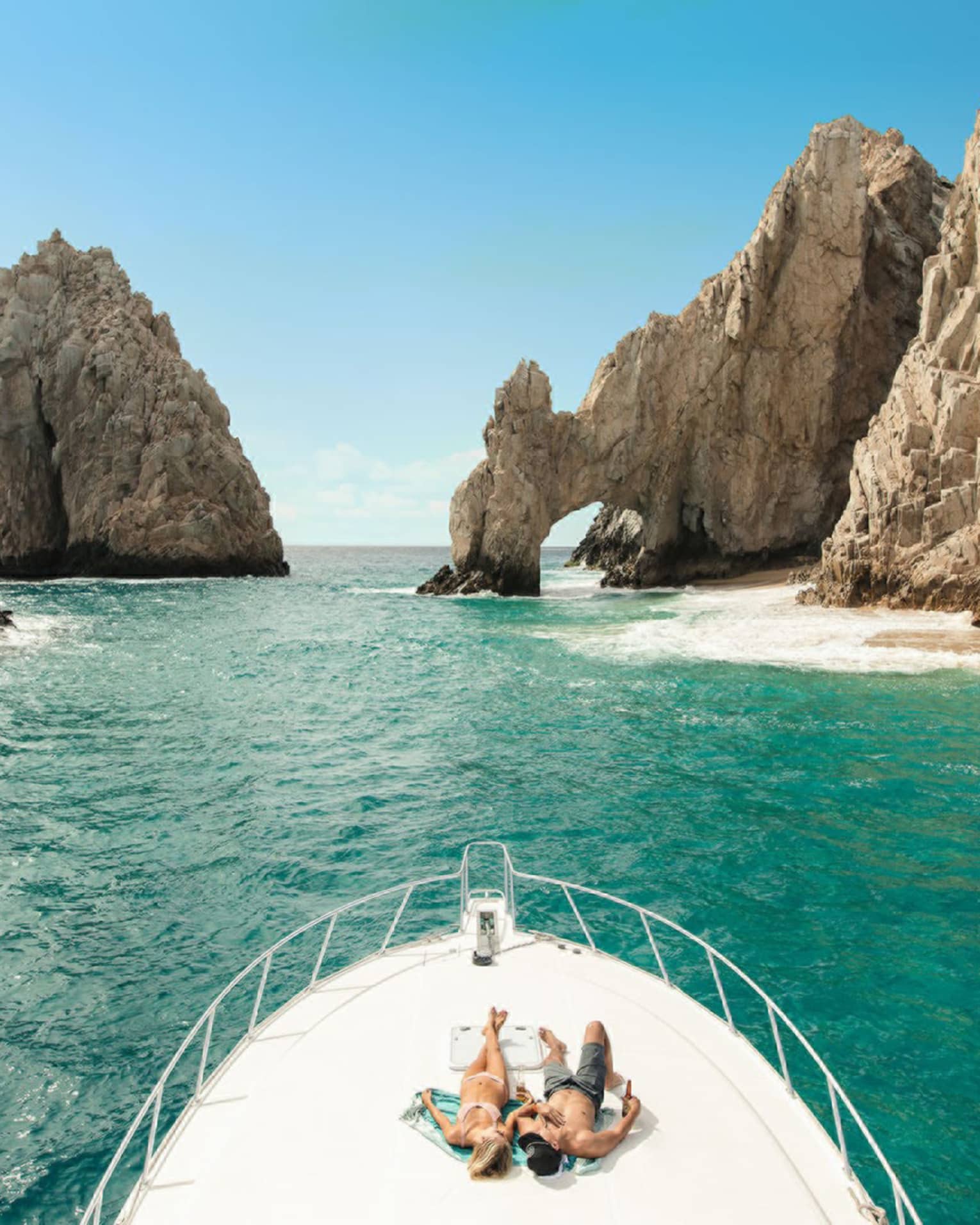 Two people lie on the front of a boat in Cabo