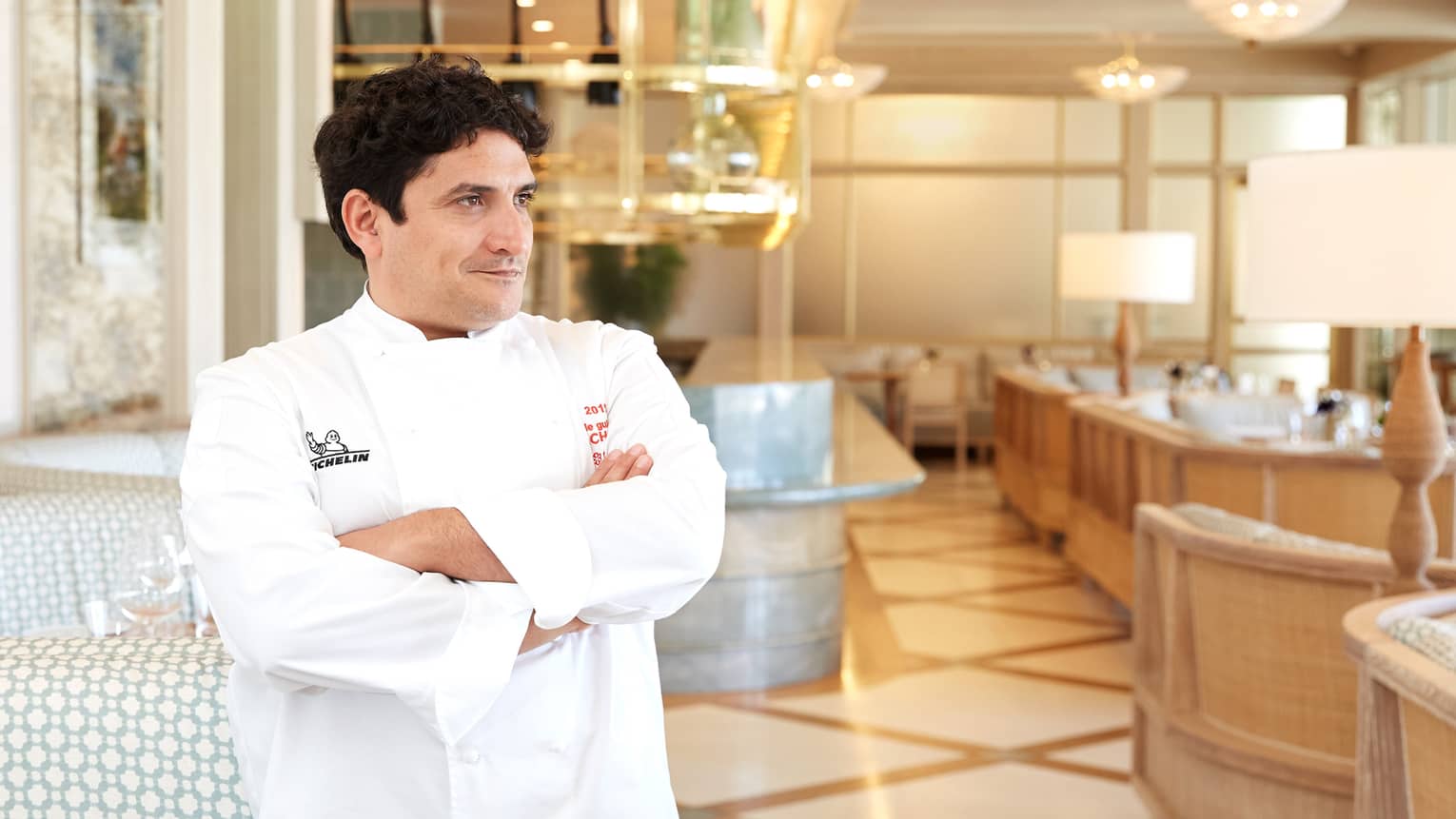 Chef crosses arms, stands in bright restaurant near dining booths