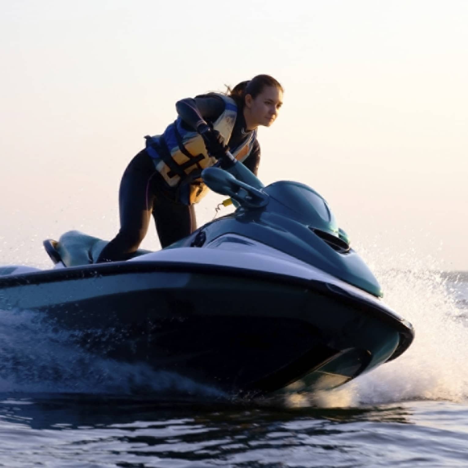 Woman wearing life jacket stands, steers jet ski on ocean at sunset