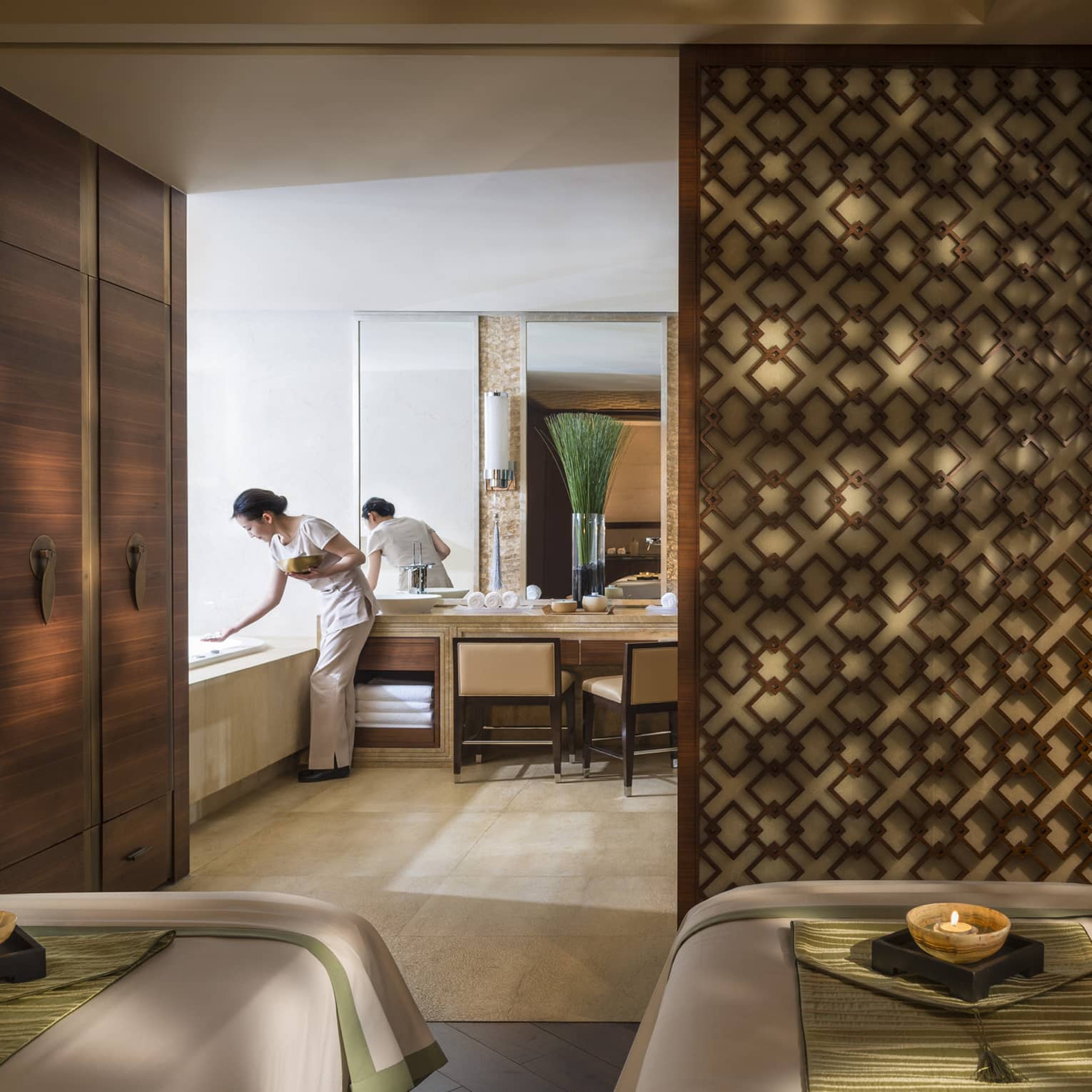 Couples massage beds side-by-side in spa room with candles and staff preparing bath