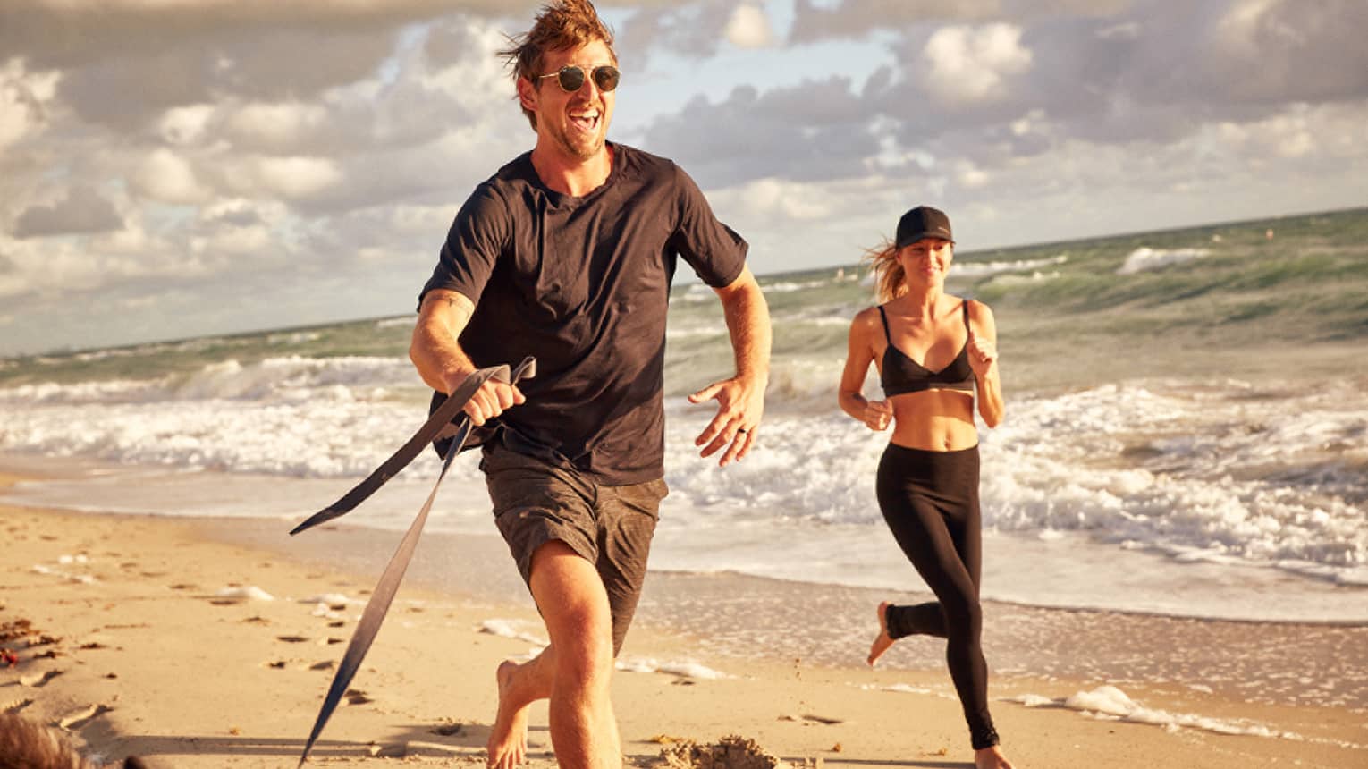 Man and woman jog along the beach with their dog